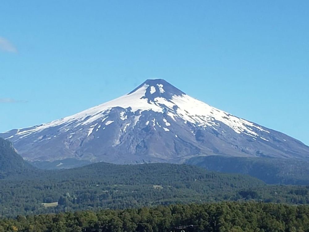 Vulcão Villarrica coberto de neve sobre a floresta, visto de Pucón