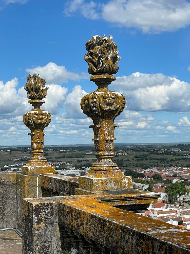 Pináculos de pedra no alto de um terraço, com a cidade de Évora abaixo