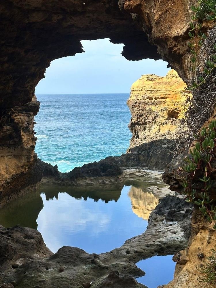 Arco de rocha com o mar ao fundo e uma poça refletindo o céu, na Great Ocean Road