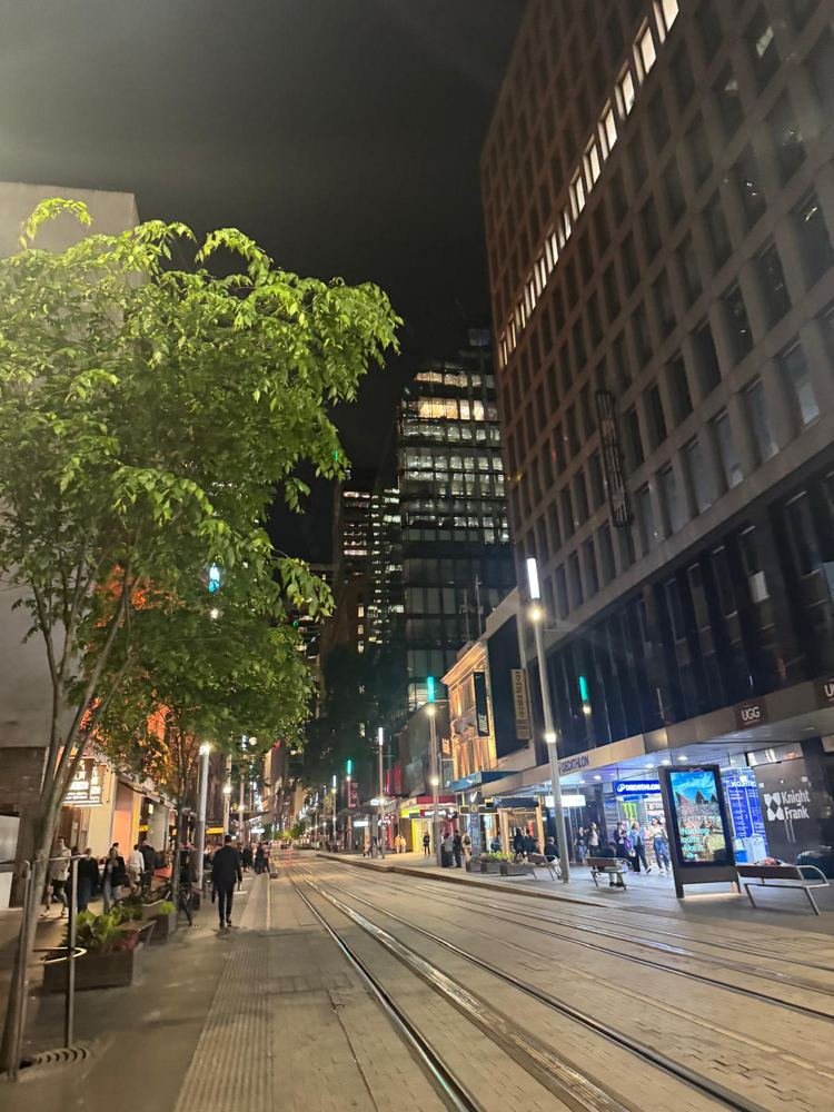 George Street à noite, no centro de Sydney, com os trilhos do VLT e os prédios iluminados